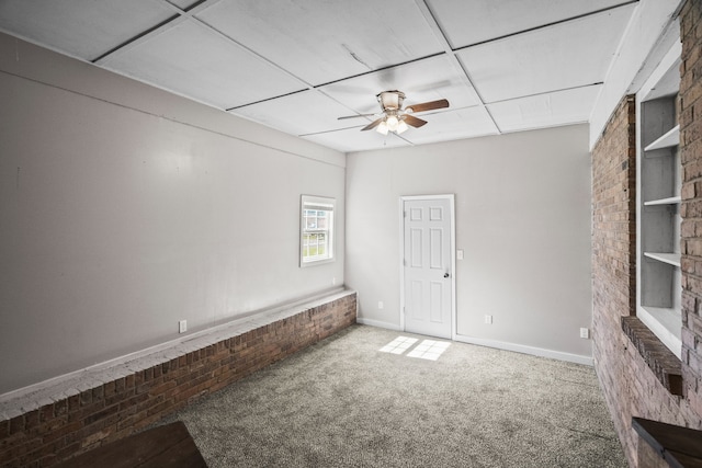 empty room featuring ceiling fan, a paneled ceiling, carpet floors, a fireplace, and built in features