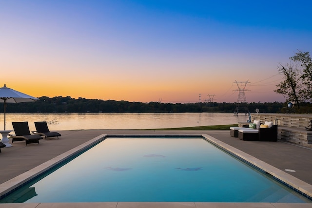 pool at dusk with a water view and a patio area