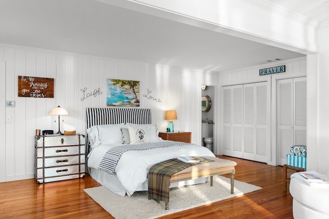 bedroom featuring crown molding, two closets, and hardwood / wood-style flooring