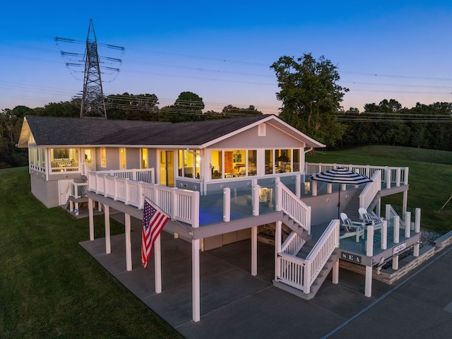 back house at dusk featuring a yard, a sunroom, a patio area, and a wooden deck