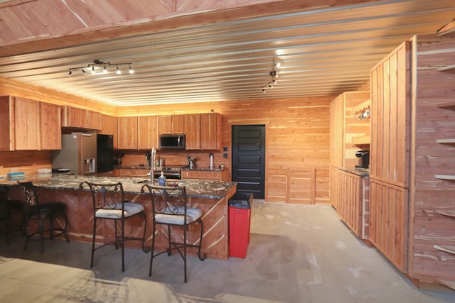 kitchen featuring wood walls, sink, stainless steel appliances, kitchen peninsula, and a kitchen bar