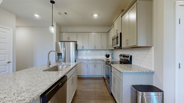 kitchen with sink, decorative light fixtures, stainless steel appliances, light stone countertops, and dark hardwood / wood-style flooring