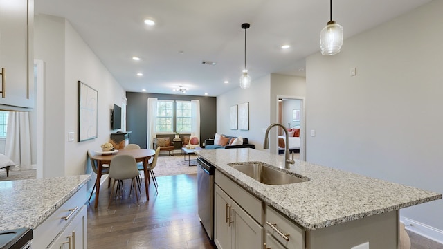 kitchen featuring sink, dark hardwood / wood-style flooring, appliances with stainless steel finishes, decorative light fixtures, and a center island with sink