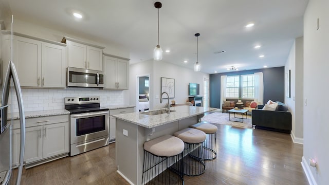 kitchen with sink, a kitchen island with sink, stainless steel appliances, dark hardwood / wood-style flooring, and decorative backsplash