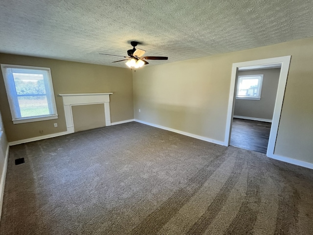 unfurnished living room featuring ceiling fan, a textured ceiling, dark carpet, and a healthy amount of sunlight