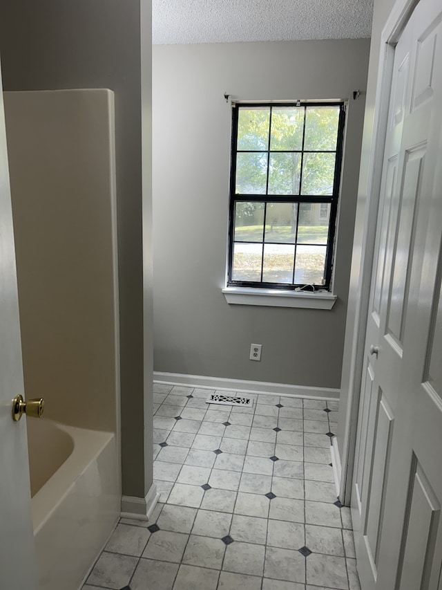 bathroom with a textured ceiling, a bath, and tile patterned floors