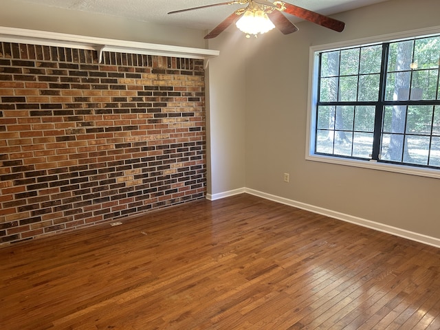 unfurnished room featuring ceiling fan, a textured ceiling, dark hardwood / wood-style floors, and brick wall