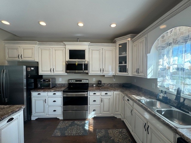 kitchen featuring dark wood-type flooring, dark stone countertops, sink, appliances with stainless steel finishes, and white cabinetry