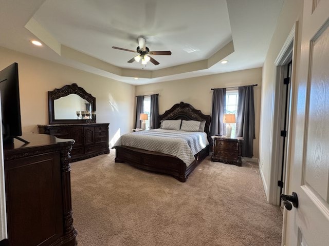 carpeted bedroom with ceiling fan and a tray ceiling