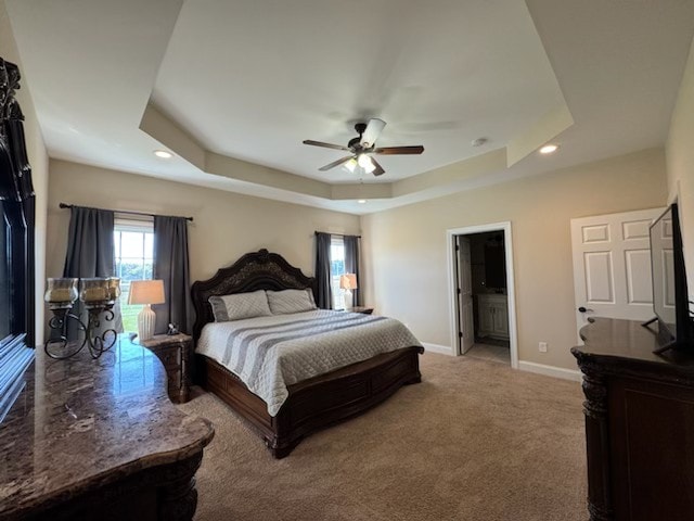 bedroom featuring light carpet, ensuite bath, ceiling fan, and a raised ceiling