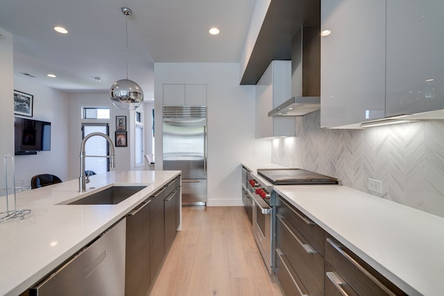 kitchen with wall chimney exhaust hood, light hardwood / wood-style floors, pendant lighting, sink, and high end appliances