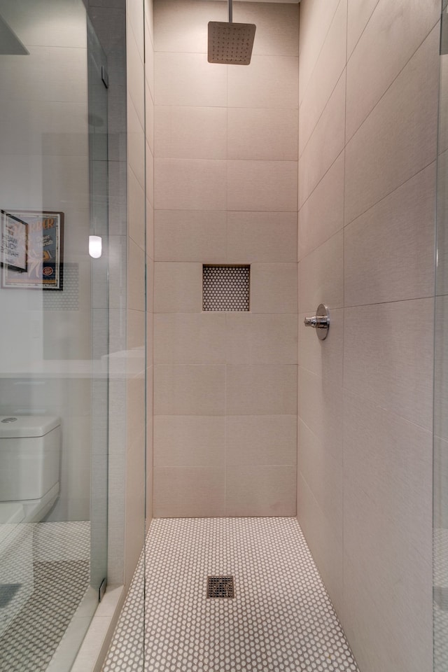 bathroom with tile patterned floors, tiled shower, and toilet