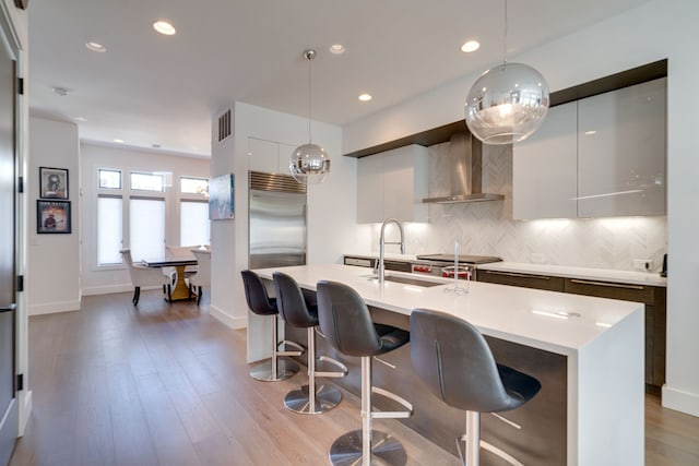 kitchen with pendant lighting, wall chimney range hood, white cabinets, and light hardwood / wood-style flooring