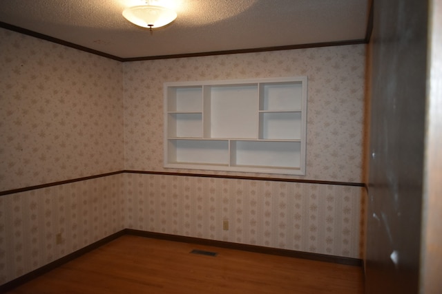 unfurnished room featuring hardwood / wood-style floors, a textured ceiling, built in features, and ornamental molding