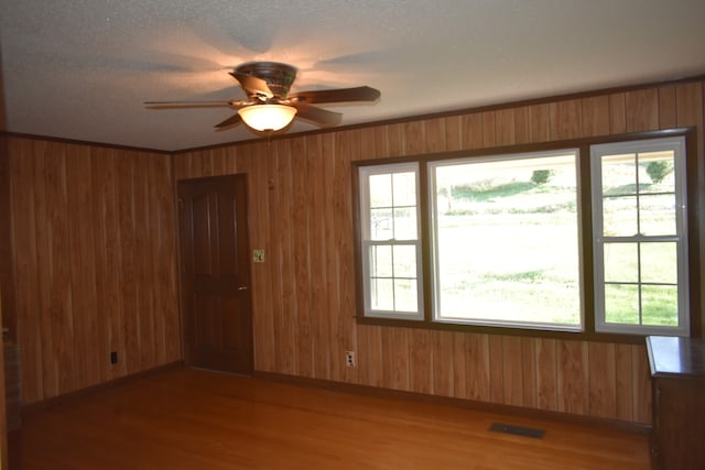 spare room featuring a wealth of natural light, ceiling fan, wooden walls, and hardwood / wood-style flooring