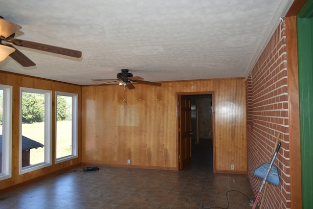 empty room with ceiling fan, ornamental molding, a textured ceiling, and wooden walls