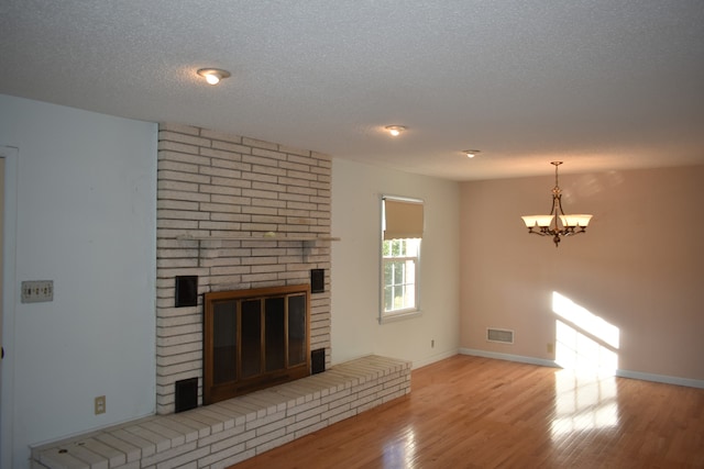 unfurnished living room featuring a chandelier, a fireplace, light hardwood / wood-style floors, and a textured ceiling