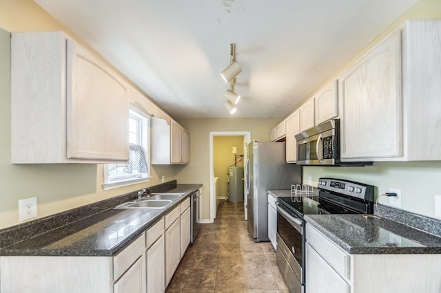 kitchen featuring rail lighting, dark stone countertops, sink, appliances with stainless steel finishes, and light brown cabinetry