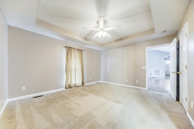 empty room featuring light carpet, a tray ceiling, and ceiling fan