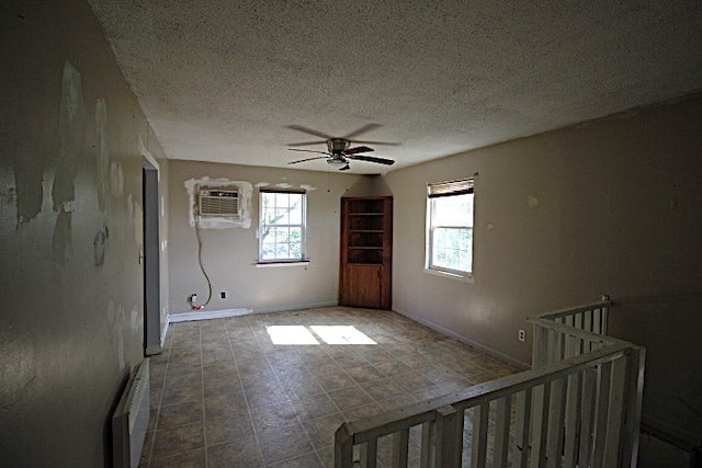 spare room featuring ceiling fan, plenty of natural light, a wall mounted air conditioner, and a textured ceiling