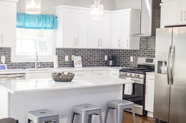 kitchen with stainless steel appliances, wall chimney range hood, decorative light fixtures, and white cabinetry