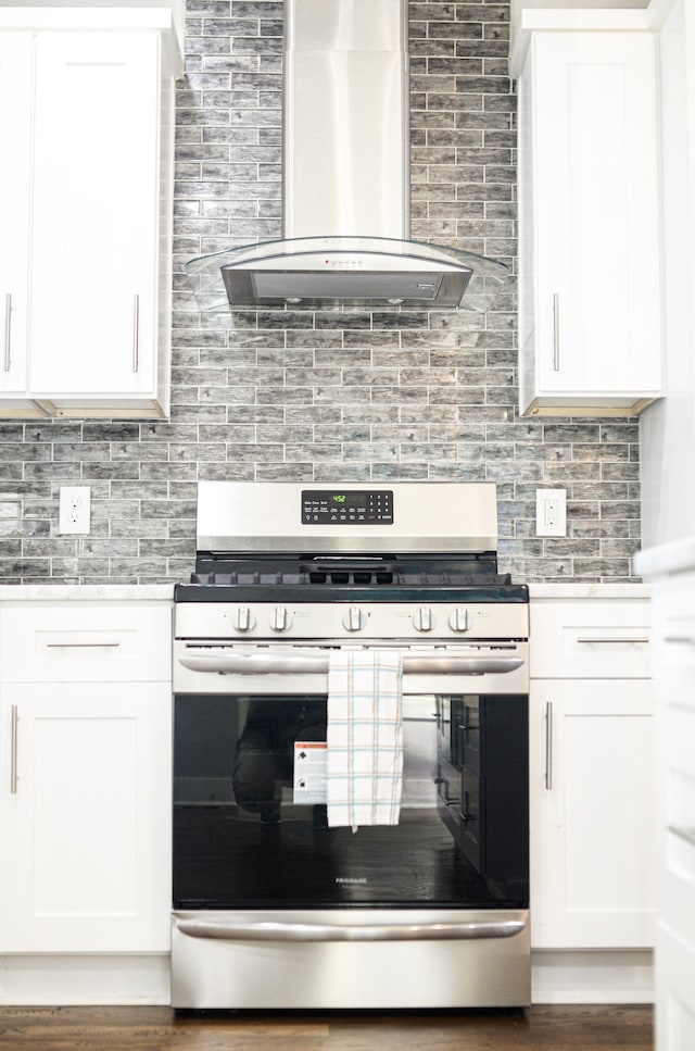 kitchen with wall chimney exhaust hood, tasteful backsplash, gas range, and white cabinets