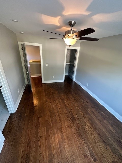 unfurnished bedroom with dark wood-type flooring, a spacious closet, a closet, and ceiling fan