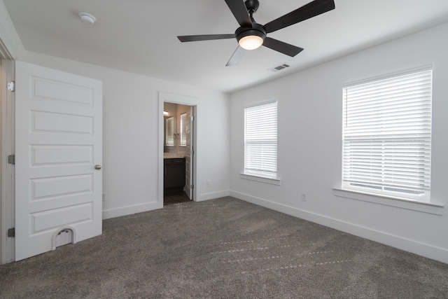 unfurnished bedroom featuring connected bathroom, dark carpet, and ceiling fan