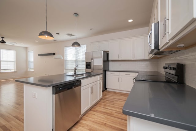 kitchen with sink, an island with sink, stainless steel appliances, decorative light fixtures, and white cabinets