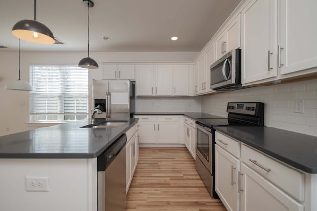 kitchen featuring an island with sink, appliances with stainless steel finishes, white cabinetry, sink, and decorative light fixtures