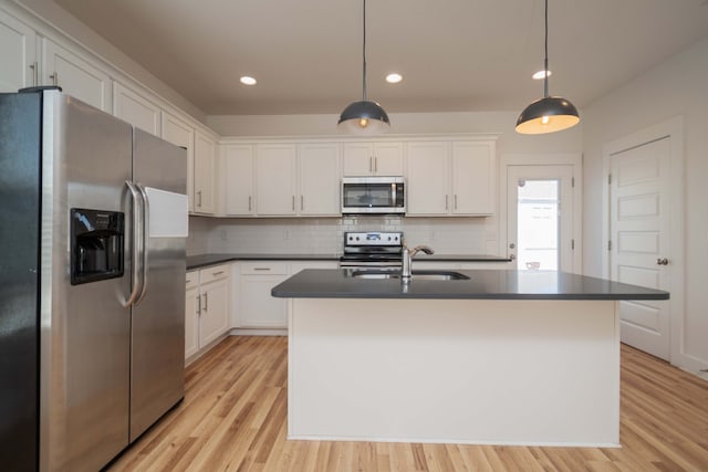 kitchen featuring light hardwood / wood-style flooring, an island with sink, white cabinets, decorative light fixtures, and appliances with stainless steel finishes