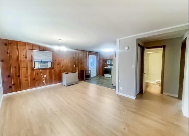 unfurnished living room featuring light wood-style flooring, cooling unit, a chandelier, wooden walls, and baseboards