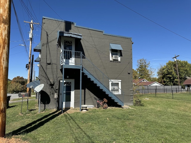 rear view of house with a yard, concrete block siding, fence, and stairway