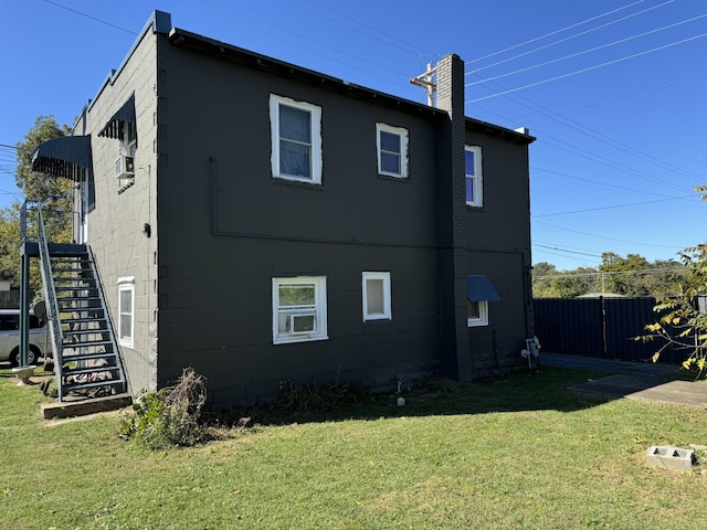 view of home's exterior featuring concrete block siding, a yard, stairway, fence, and a chimney