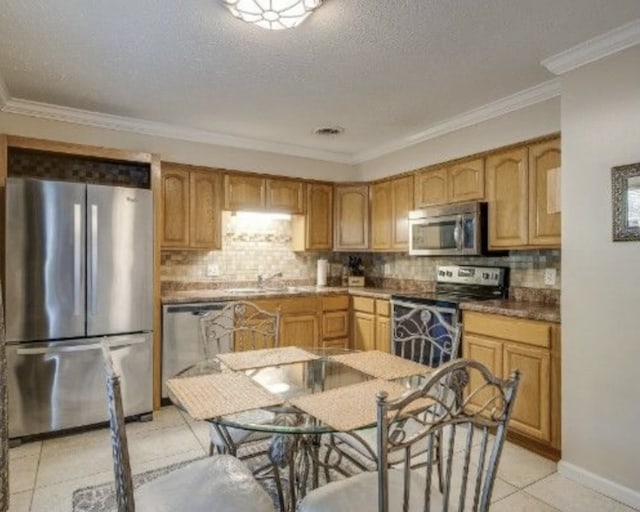 kitchen with tasteful backsplash, ornamental molding, appliances with stainless steel finishes, light tile patterned floors, and a textured ceiling