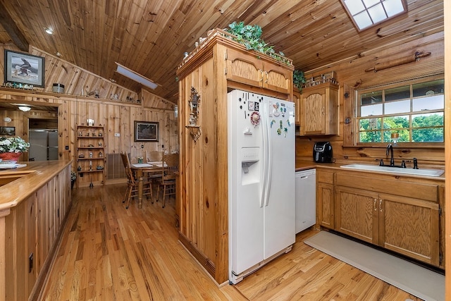 kitchen with light hardwood / wood-style floors, wood walls, sink, and white appliances