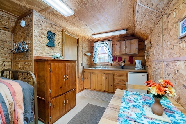 kitchen with wood walls, sink, white dishwasher, and vaulted ceiling