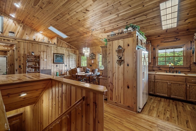 kitchen with wood ceiling, white fridge with ice dispenser, light hardwood / wood-style flooring, sink, and wood walls