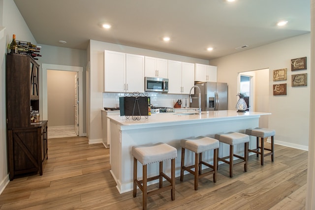 kitchen with a kitchen island with sink, light wood-type flooring, a breakfast bar, stainless steel appliances, and white cabinets