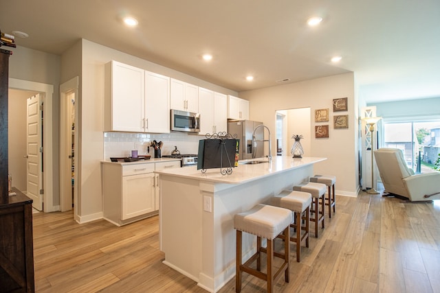 kitchen with a center island with sink, light wood-type flooring, stainless steel appliances, and white cabinets