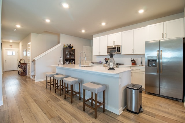 kitchen with an island with sink, white cabinets, sink, light hardwood / wood-style flooring, and appliances with stainless steel finishes