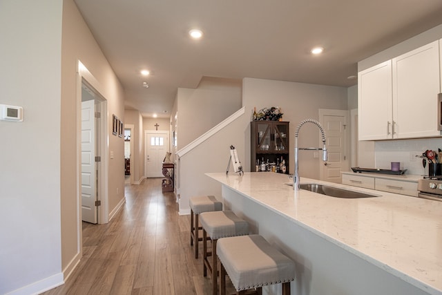 kitchen featuring light hardwood / wood-style flooring, a breakfast bar, sink, light stone countertops, and white cabinets