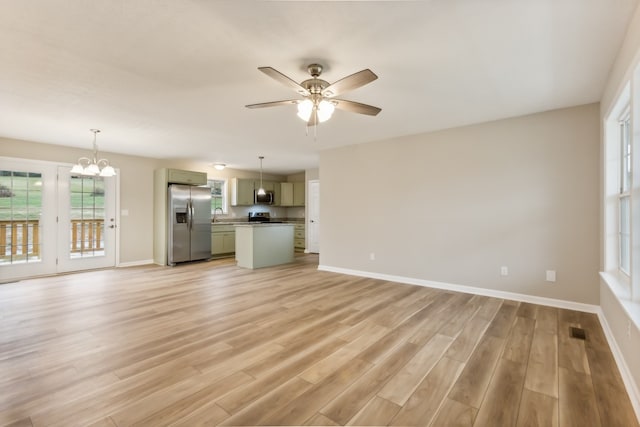 unfurnished living room featuring ceiling fan with notable chandelier and light hardwood / wood-style flooring