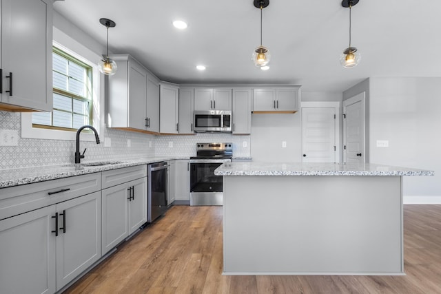 kitchen featuring sink, hanging light fixtures, appliances with stainless steel finishes, a kitchen island, and light stone countertops