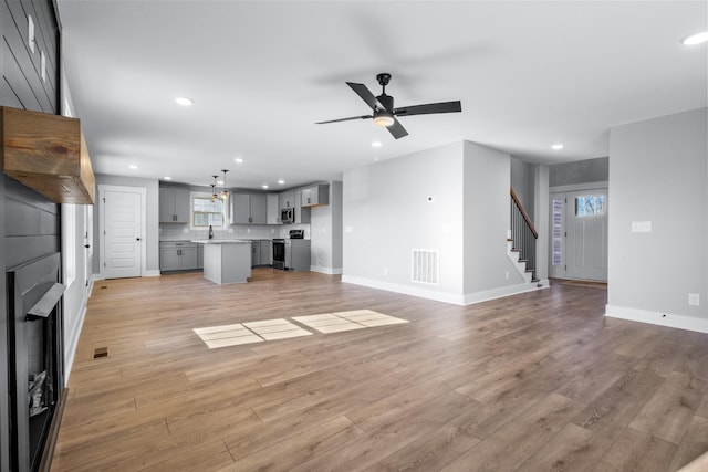 unfurnished living room featuring ceiling fan, sink, a large fireplace, and light hardwood / wood-style floors