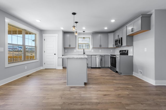 kitchen featuring gray cabinetry, decorative light fixtures, a kitchen island, stainless steel appliances, and backsplash