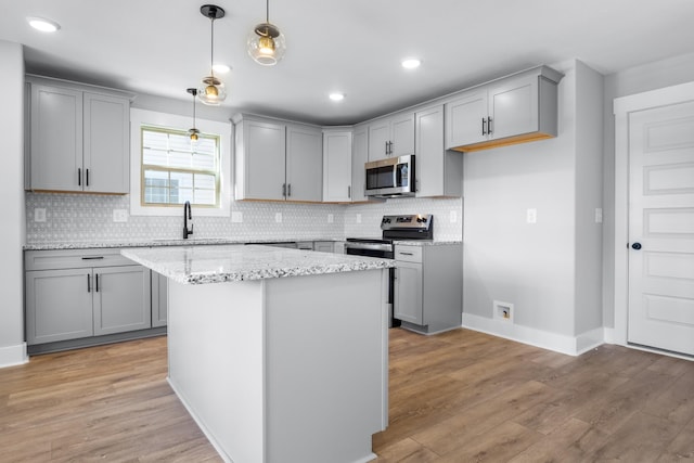 kitchen featuring appliances with stainless steel finishes, hanging light fixtures, light stone counters, light hardwood / wood-style floors, and a kitchen island