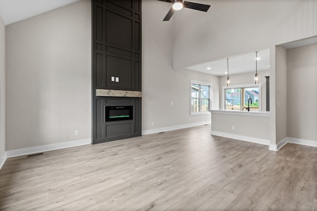 unfurnished living room featuring lofted ceiling, sink, light hardwood / wood-style flooring, ceiling fan, and a large fireplace