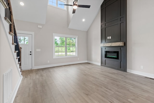 unfurnished living room featuring a high ceiling, ceiling fan, light wood-type flooring, and a fireplace