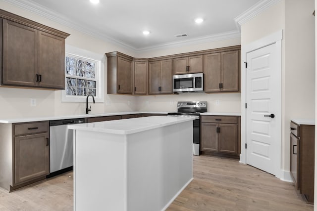 kitchen featuring sink, ornamental molding, a kitchen island, stainless steel appliances, and light hardwood / wood-style floors